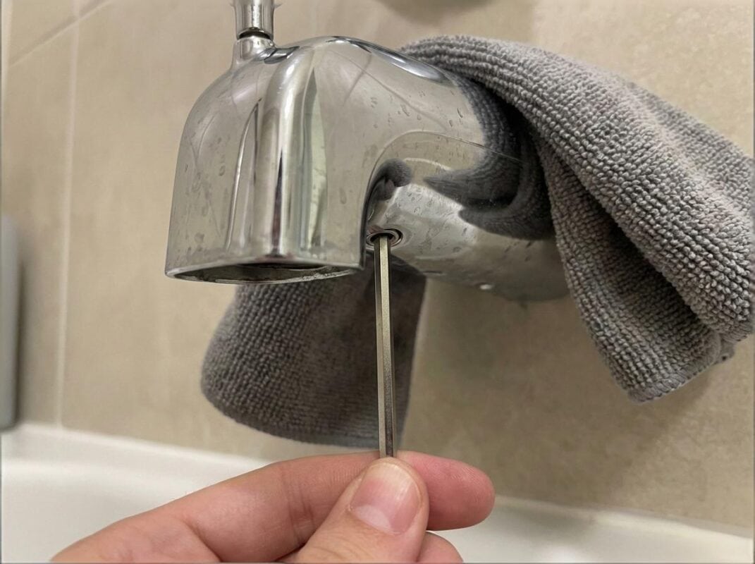 Close-up of an Allen key loosening the hidden set screw on the underside of a slip-on bathtub spout.