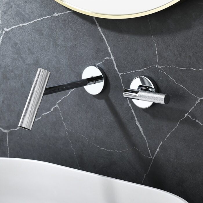Brushed nickel bathroom faucet and handle on dark gray marble wall with white bathtub beneath.