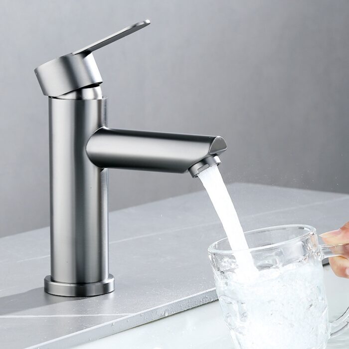 Shiny modern stainless steel kitchen faucet with water flowing into a glass mug.