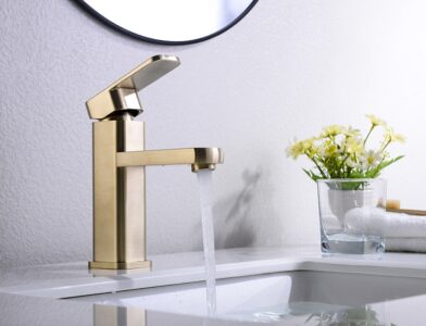 Brass bathroom faucet with water flowing, modern sink design, skincare, and floral decor in the background.