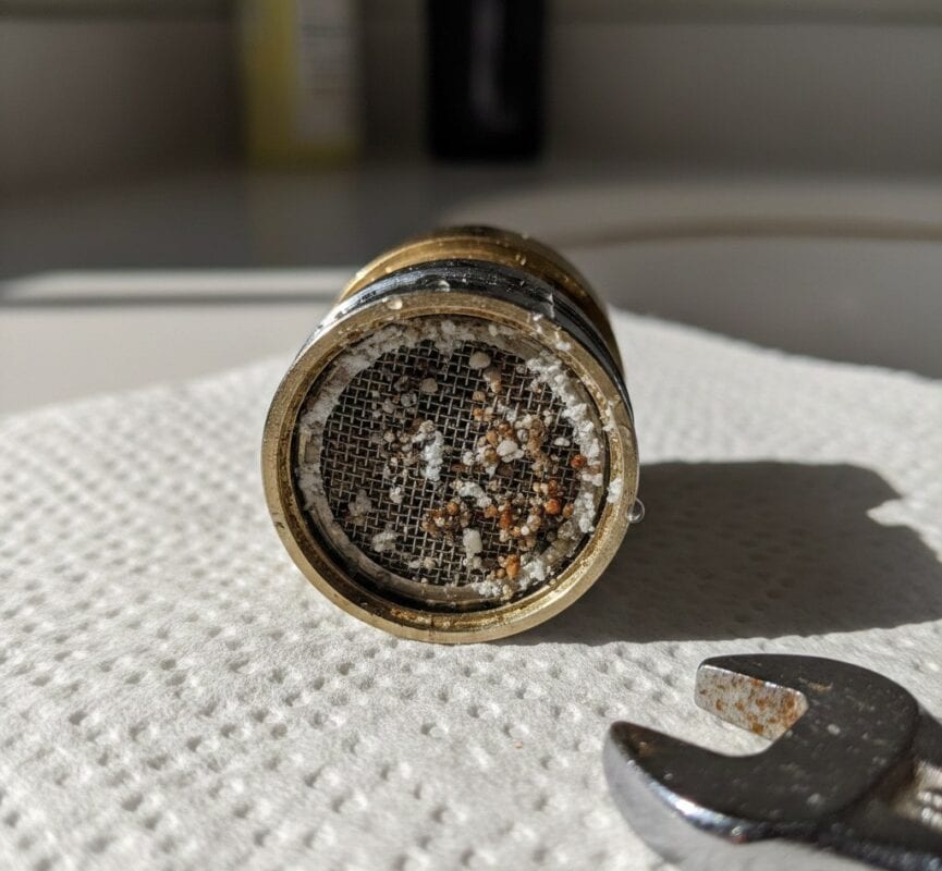 Por que a água da minha torneira está turva? Causas, segurança e correções 5 Clogged kitchen faucet aerator with mineral deposits and debris.
