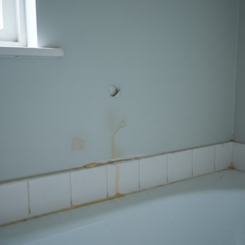 Signs of hidden water damage near a bathtub: peeling paint, swollen baseboard, and damp stain
