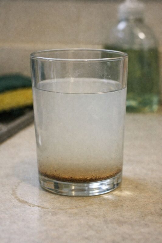 Por que a água da minha torneira está turva? Causas, segurança e correções 7 Glass of cloudy water with visible sediment settling at the bottom after standing